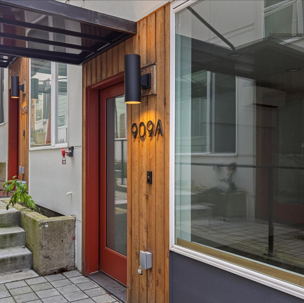 Modern dwelling entrance with red door, "909A" address, wood paneling, and sleek black lighting.