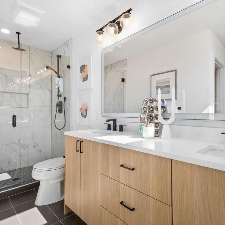 Modern bathroom with a light wood vanity, white Oscar Surfaces countertop, and glass-enclosed, marble-tile shower.