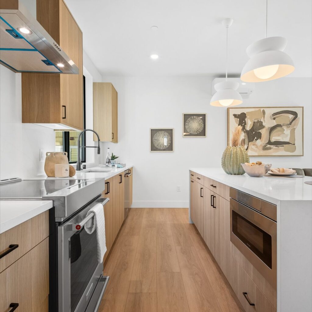 Modern kitchen with light wood cabinets, white Oscar Surfaces countertops, an island, and stainless steel appliances.