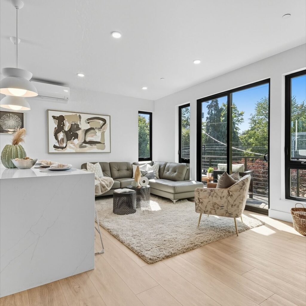 Modern living room with a gray sofa, light wood floors, and a white marble waterfall kitchen island.
